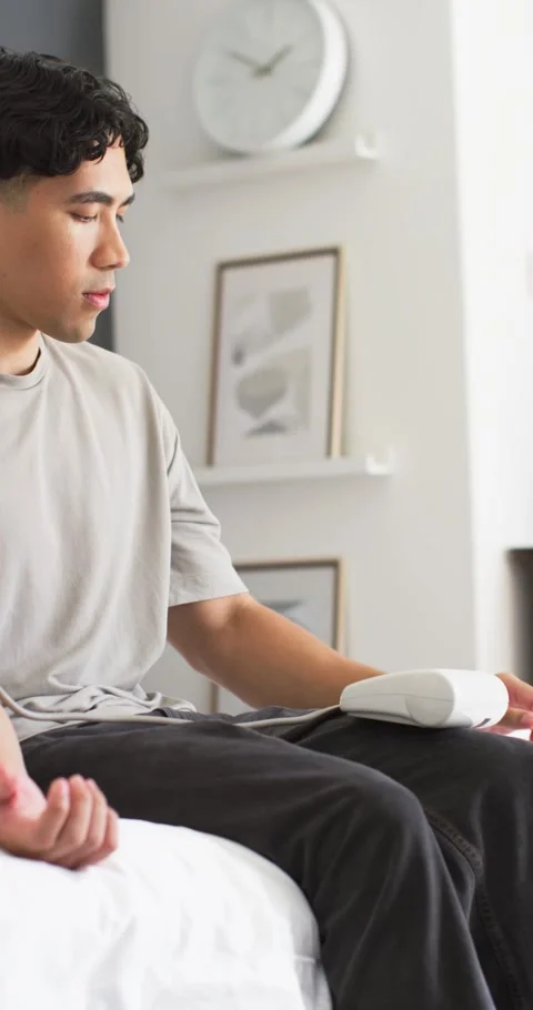 Man sitting on bed in bedroom adjusting light blue blood pressure cuff and white Stock Footage 345219498