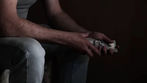 Man sitting on a bed in a dark room counting money, 100 american dollars banknot Stock Footage 129820762