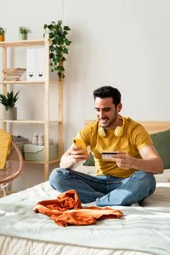 Man sitting on bed doing online shopping with smart phone. Stock Photos