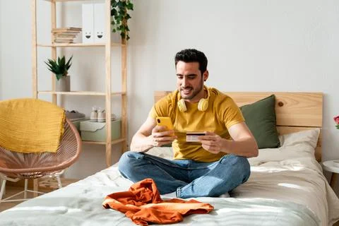Man sitting on bed doing online shopping with smart phone. Stock Photos