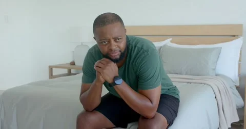 Man sitting on bed edge in bedroom, leaning, contemplating, shifting gaze right, Stock Footage 340070187