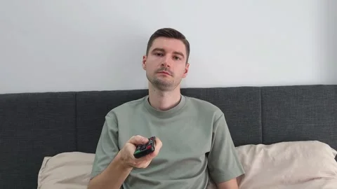 Man sitting on bed holding remote control and looking at television Stock Footage 284044196