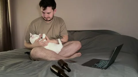 Man sitting on bed with laptop, playing with white cat Stock Footage 310511351