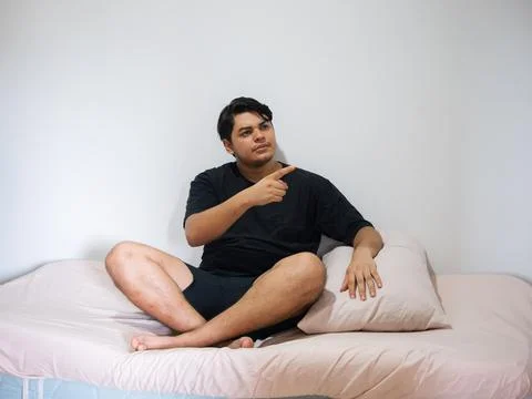 Man sitting on bed pointing to side in bedroom Stock Photos