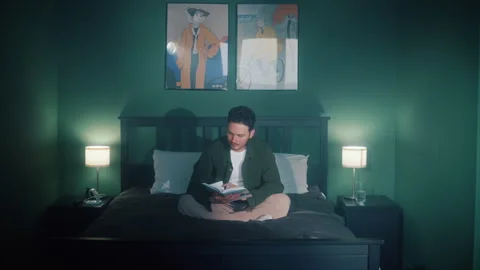 Man sitting in bed reading book at night in cozy bedroom 스톡 동영상 319544092