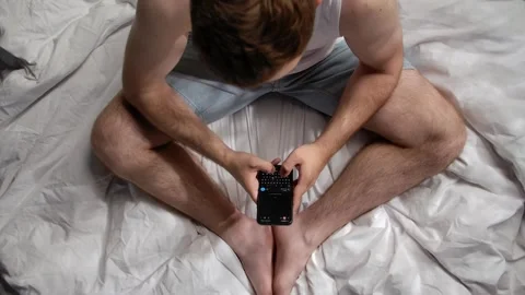 Man Sitting on Bed While Using Smartphone Device Stock Footage 311455519