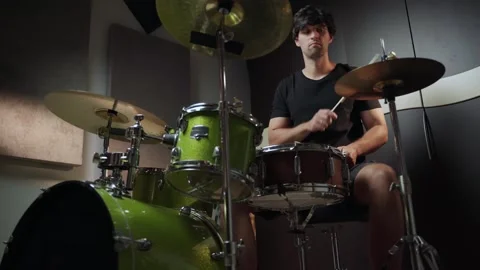 A man is sitting behind a drum set, playing the drums. He is wearing a black t Stock Footage 280964834