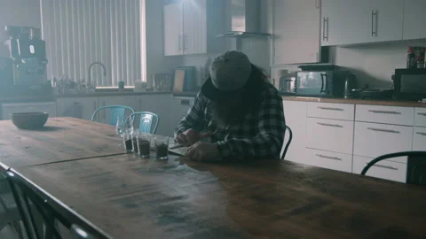 Man sitting behind kitchen table writing on a piece of paper Video stock 131234622