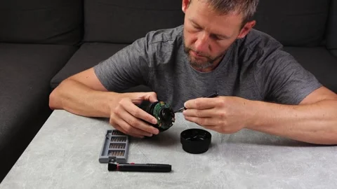 Man sitting behind table and repair, cleaning broken camera lens with screw.. Stock Footage 315681705