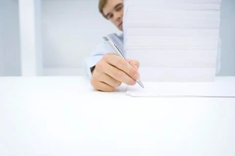 Man sitting behind tall stack of documents, writing on single sheet of paper Foto stock