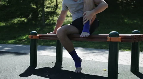 A man sitting on a bench and putting off an ankle support Stock Footage 67626758