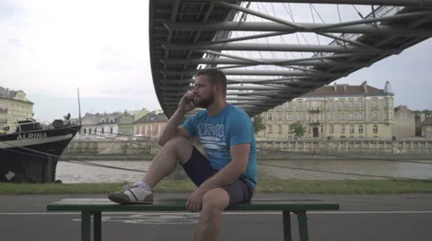 Man sitting on the bench and talking by cellphone, against the river. Vidéo 65187689