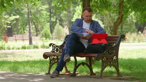 Man Sitting on the Bench and Working Outdoors. Vidéo 132010195