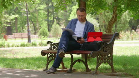 Man Sitting on the Bench and Working Outdoors. 库存影片 132011458