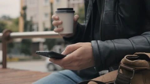 Man sitting on bench in the city centre drinking coffee and use a smartphone Stock Footage 131460668