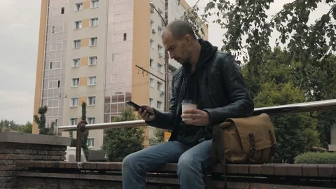 Man sitting on bench in the city centre drinking coffee and use a smartphone Stock Footage 131602962