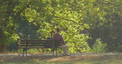 Man is Sitting on The Bench Man Has Leaned His Arms to Knees Backpack is on the Video stock 56064502