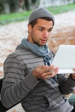 Man sitting on a bench with netbook pulling face Stock Photos