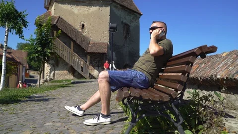 Man sitting on the bench in the old town and chatting on cellphone Stock Footage 103502017