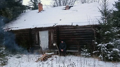 Man Sitting on Bench Outside Small Wooden House in Snowy Forest Stock Footage 334239337