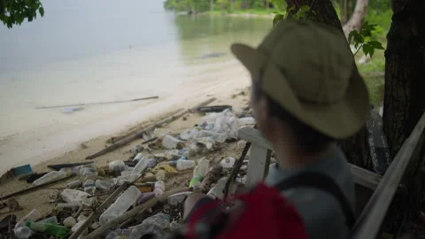Man sitting on bench overlooking a sandy beach polluted 動画素材 344700509