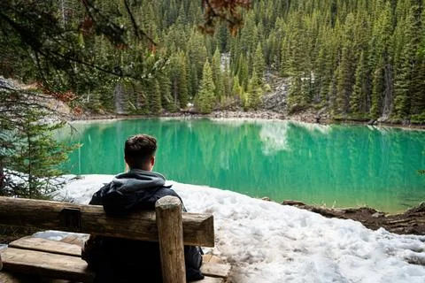 Man sitting on a bench overlooking a turquoise alpine lake Stock Photos