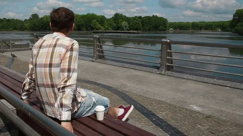 The man is sitting on a bench in the park and drinking coffee Stockbeeldmateriaal 76127818