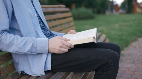 A man sitting on a bench in a park and reading a book, turning the page Stock Footage 129558110