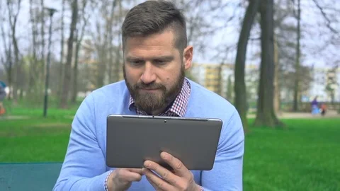 Man sitting on bench in park browsing tablet computer, close portrait steadicam Stock Footage 74344503