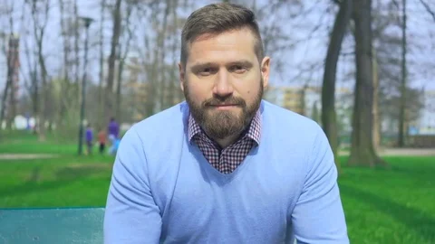 Man sitting on bench in park looking at camera, close portrait steadycam Vídeo Stock 74344456
