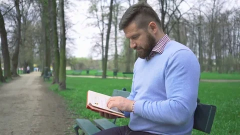 Man sitting on bench in park reading book, steadycam shot Vídeo Stock 74344257