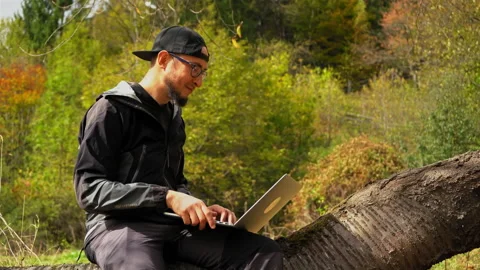 A man sitting on a bench reading a book. Young man works behind a laptop in the Video stock 139871899