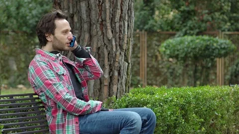 Man sitting on a bench talking on the phone with a friend happily Stock Footage 72309815