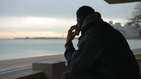 Man is sitting on the bench talking on the phone and looking at the sea Video stock 82653446