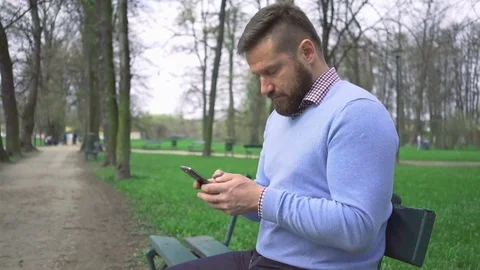 Man sitting on bench typing message by smartphone app, look at camera, steadycam 動画素材 74344247