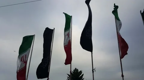 A Man sitting on a bench under Iranian and black flag of Islam, waving in wind Stock Footage 58952392