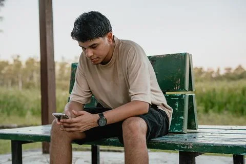 Man sitting on a bench using a smartphone outdoors Stock Photos