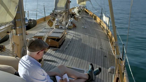 Man sitting on boat drawing on small notebook with castle in background Video stock 235365792