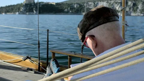 Man sitting on boat drawing on small notebook with castle in background 스톡 동영상 235366194