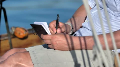 Man sitting on boat drawing on small notebook 스톡 동영상 235369672