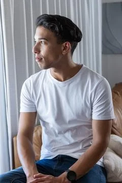Man sitting on brown leather sofa looking toward window with vertical blinds, Stock Photos