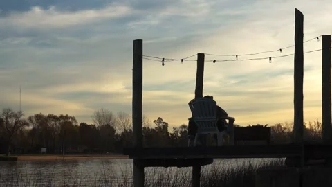 Man sitting in a cabin pier looking at the river and sky at sunset Stock Footage 196447647