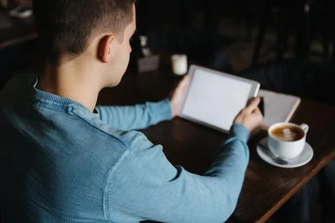 Man is sitting in a cafe and using a tablet. Student spend time in cafe and Stock Photos