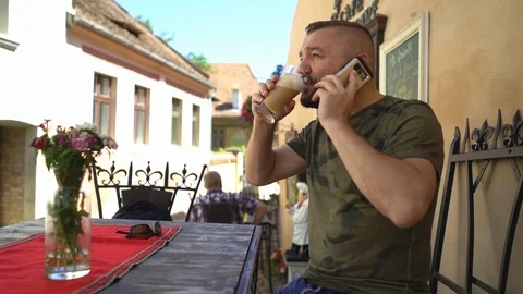 Man sitting in the cafe with coffee in the old town and talking on cellphone Stock Footage 103502333