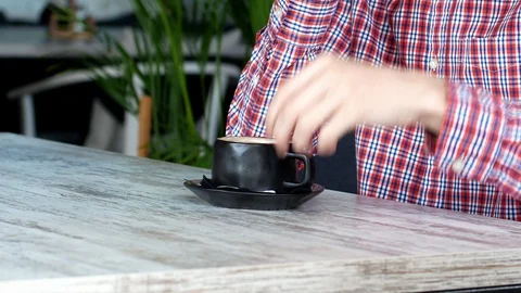 The man is sitting in a cafe with a cup of coffee mixing it. Stock Footage 111728785
