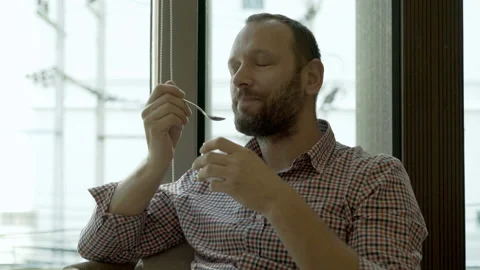 Man sitting in the cafe next to the window and eating yoghurt Stock Footage 88436459