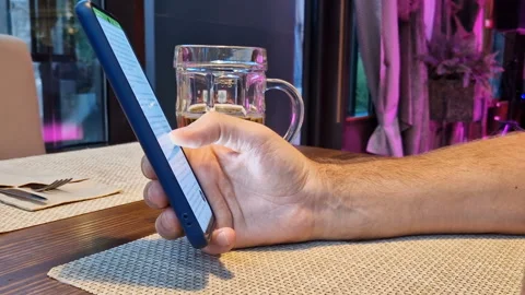 A man is sitting in a cafe with a phone, drinking beer. Video stock 240716508