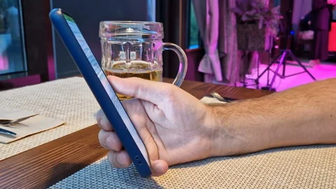A man is sitting in a cafe with a phone, drinking beer. Stock Footage 240717963