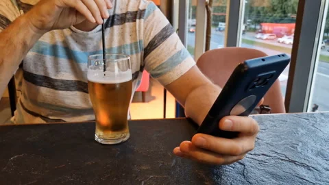 A man is sitting in a cafe with a phone, drinking beer. Stock Footage 241015749