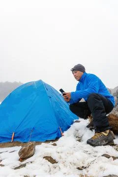 A man sitting in camping tent, using smartphone Stock Photos